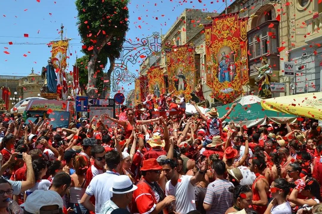 Reference photograph: A festa crowd in red celebrating beneath a statue, beside the paper model rebuilt from it